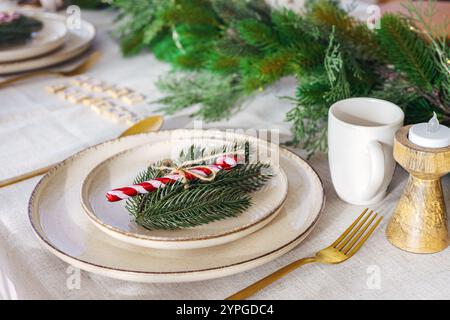 Wunderschön gestalteter Esstisch für die Weihnachtsfeier, mit eleganten Tellern, goldenem Besteck und frischem Grün. Zuckerrohr sorgt für eine fröhliche Note Stockfoto