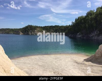 Eine einladende Seeszene mit ruhigem, klarem Wasser, umgeben von üppig grünen Bäumen. Die Sandküste bietet einen ruhigen Ort zum Entspannen unter Stockfoto