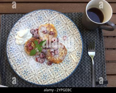 Ein herrliches Frühstücksrestaurant mit süßen Pfannkuchen mit Puderzucker und frischen Beeren, begleitet von einer Tasse Kaffee. Das Essen wird serviert Stockfoto