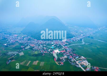 Blick aus der Vogelperspektive auf den nebeligen Morgen mit Vorstadtdorf auf üppigem Ackerland und Bergkette im Bac Son Valley in lang Son, Vietnam Stockfoto