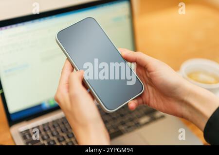 Frau Hände halten Smartphone Show Screen Laptop im Hintergrund Zuhause Kaffeetasse Stockfoto