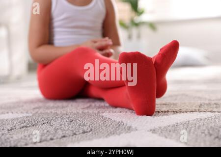 Kind in roten Strumpfhosen sitzt zu Hause auf dem Boden, Nahaufnahme Stockfoto