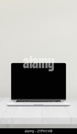 Laptop mit leerem Bildschirm auf einem Schreibtisch vor einer weißen Wand, ideal für Mockup-Präsentationen von Websites Stockfoto