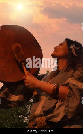 Eine Schamanin führt ein Ritual mit einem Tambourin bei Sonnenuntergang im Wald durch. Schamanisches Ritual. Ethnische Traditionen Stockfoto