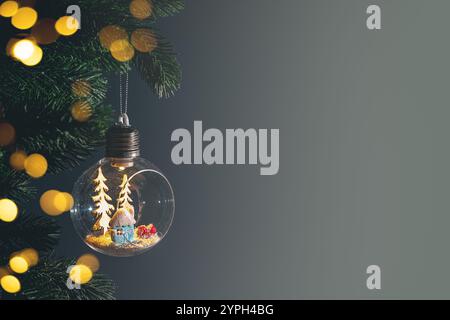 Glühlampen-Ornament mit Miniatur-schneebedecktem Haus und Bäumen, die an weihnachtsbaumzweigen vor dunklem Hintergrund hängen. Kopierbereich, Begrüßung ca. Stockfoto