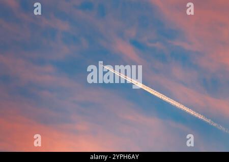 Ein Jet-Flugzeug hinterlässt einen Kondensstreifen am Abendhimmel mit Zirruswolken. Landschaft bei Sonnenuntergang. Stockfoto