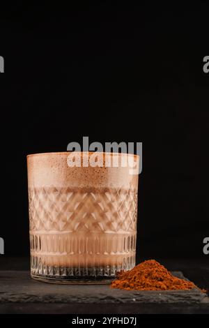 Schokoladenmilchshake mit Schlagsahne, serviert in einem Glas auf einem schwarzen Tisch. Trinken Sie aus nächster Nähe Stockfoto