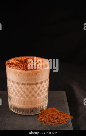 Heiße Schokolade mit Milchschaum, belegt mit Schokoladenpulver, serviert in einem transparenten Glas, isoliert auf schwarzem Hintergrund Stockfoto