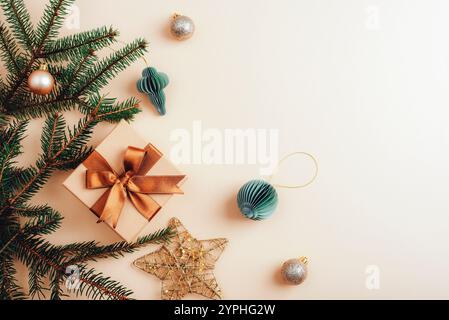 Weihnachtsgeschenkkasten mit Bronzeband und Goldschmuck, Tannenzweigen auf beigefarbenem Hintergrund. Draufsicht, flach, Kopierbereich. Stockfoto