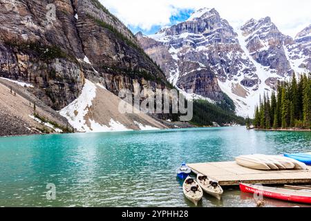 Ein wunderschöner See mit einem Dock und mehreren Kajaks. Das Wasser ist blau und die Berge im Hintergrund sind mit Schnee bedeckt Stockfoto