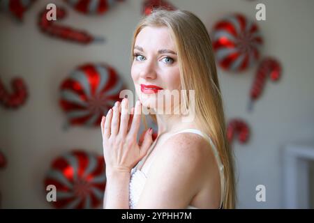 Porträt der schönen blonden Frau. Der Hintergrund ist mit rot-weiß gestreiften Ballons im Bonbonmotiv dekoriert Stockfoto