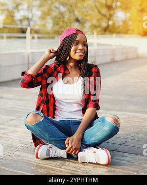 Eine junge afrikanerin, die Spaß im Stadtpark hat, mit einem roten karierten Hemd und einer Kappe Stockfoto