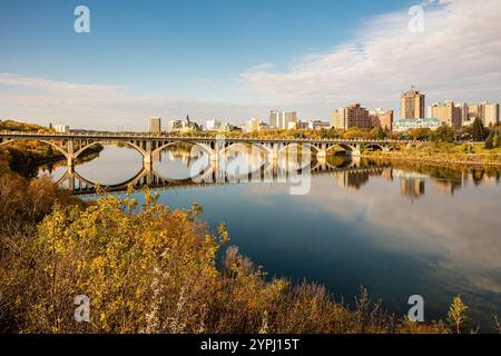 Eine Brücke überspannt einen Fluss mit einer Stadt im Hintergrund. Das Wasser ist ruhig und der Himmel ist klar Stockfoto