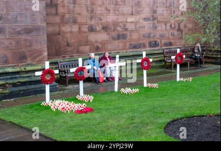 Die Menschen sitzen nach dem Gedenktag im Garten der Chester Cathedral Cheshire zwischen Mohnkreuzen. Stockfoto