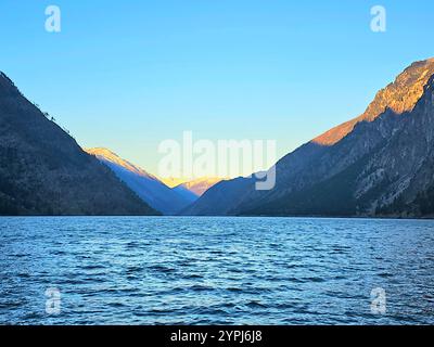 Sonnenaufgang über einem friedlichen See mit Bergen, die sich im stillen Wasser spiegeln Stockfoto