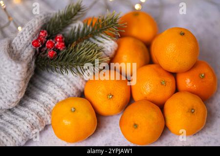 Frische Mandarinen mit einem gemütlichen Strickschal, roten Beeren und grünen Tannenzweigen auf weichem Hintergrund mit warmen Lichtern Stockfoto