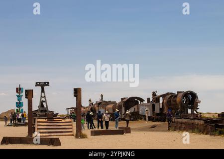 Touristen erkunden den Bahnfriedhof (Cementerio de Trenes) in der Nähe von Uyuni, Bolivien, mit rostigen Lokomotiven und Industrieskulpturen. Stockfoto