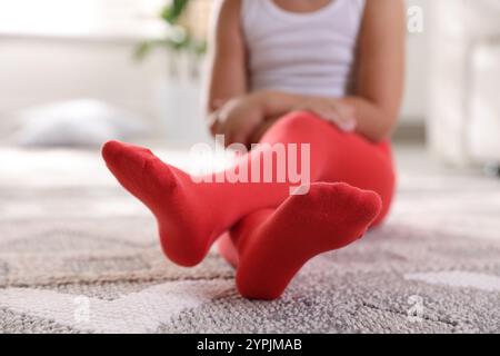 Kind in roten Strumpfhosen sitzt zu Hause auf dem Boden, Nahaufnahme Stockfoto