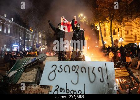 Tiflis, Georgien. Dezember 2024. Pro-europäische Demonstranten posieren mit der georgischen Flagge von oben auf einer Barrikade bei einem Protest gegen die Regierung. Auf dem Schild unter ihnen steht: „Go on Strike!“. Quelle: Jay Kogler/Alamy Live News Stockfoto