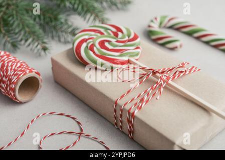 Weihnachtshintergrund. Geschenkbox verpackt in Bastelpapier mit grünem und rotem Lutscher und Kiefernzweig auf hellem Hintergrund. Stockfoto