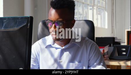 Vorderansicht eines jungen schwarzen Geschäftsmannes, der an einem Desktop-pc in einem modernen Büro arbeitet Stockfoto