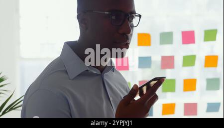 Seitenansicht eines jungen schwarzen Geschäftsmannes, der in einem modernen Büro auf dem Handy spricht Stockfoto