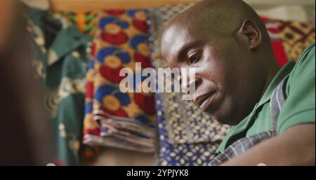 Seitenansicht eines afrikanischen Schneiders in einer Werkstatt in der Gemeinde, die mit bunten Stoffen arbeitet Stockfoto