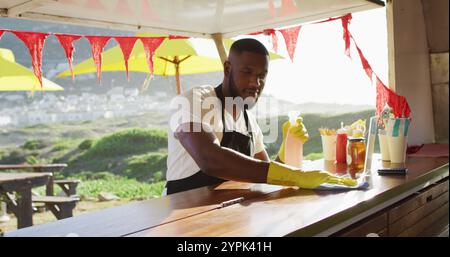 afroamerikaner mit Schürze und Handschuhen, der den Food Truck mit Desinfektionsspray reinigt Stockfoto