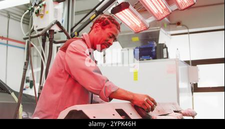 Afroamerikanischer Automechaniker, der in einer Werkstätte in der Gemeinde arbeitet, mit einem Schleifgerät an einem Stück A C Stockfoto