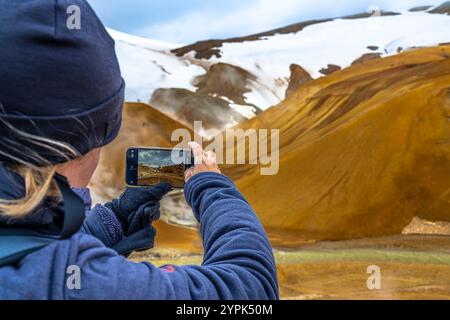 Eine Frau mit blauem Hut fotografiert die rauchigen, nebeligen Hänge des Laki-Vulkans in Island und fängt geothermische Wunder und raue vulkanische Schönheit ein. Stockfoto
