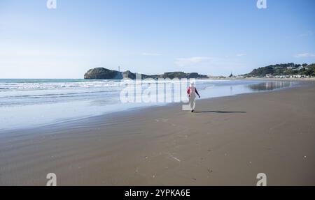 Frau, die am Castlepoint Beach läuft. Castlepoint Leuchtturm in der Ferne. Wairarapa. Neuseeland. Stockfoto