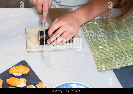 Hände eines Kindes, das eine Sushi-Rolle schneidet Stockfoto