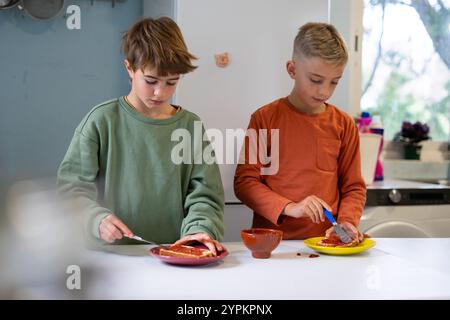 Zwei kaukasische Kinder verteilen Marmelade auf Toast in der Küche zu Hause Stockfoto