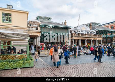 An der historischen Kolonnade des Covent Garden Market versammeln sich Menschenmassen, mit viktorianischem Eisenwerk und dem Kopfsteinpflaster plaza, die eine lebhafte Shopping-Atmosphäre schaffen Stockfoto