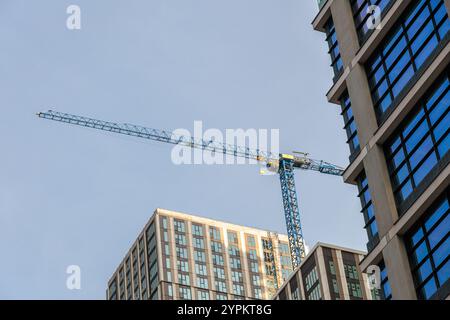 Der Baukran ragt über modernen Wohngebäuden in Canary Wharf und hebt die laufende Stadtentwicklung vor klarem blauem Himmel hervor Stockfoto