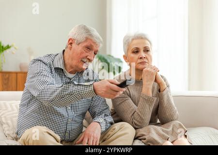 Glückliche alte Familie zu Hause. Älteres Paar, Ehemann, Frau, die auf dem Sofa im Wohnzimmer fernsieht. Eine alte, reife Familie genießt ein gemeinsames Wochenende. Großeltern schauen Fernsehen. Freizeitaktivitäten Stockfoto