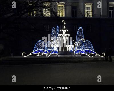 Abendlicher Blick auf eine wunderschöne Kombination in weiß und Blau von verschiedenen Beleuchtungskörpern auf einem alten Brunnen vor Neujahr, Sofia, Bulgarien Stockfoto