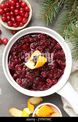 Leckere Preiselbeersoße in Soße, Beeren, Orangenschalen und Tannenzweige auf grauem Tisch, flach gelegen Stockfoto