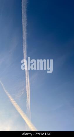 Zwei Kondensstreifen, die als lange weiße Streifen erscheinen, sind vor einem klaren, blassblauen Himmel sichtbar. Die Kondensstreifen weisen leichte Abweichungen in auf Stockfoto