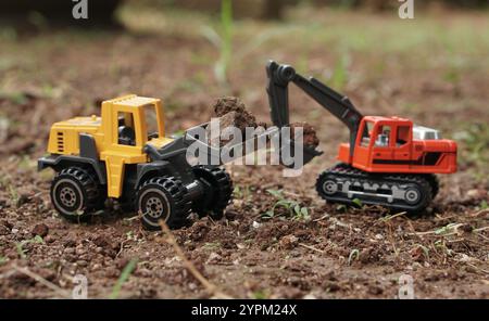 Spielzeug-Fotografie, Bagger und Radlader arbeiten zusammen, um Boden auf dem Boden im Freien zu laden. Aushubarbeiten am Baustellenkonzept. Stockfoto
