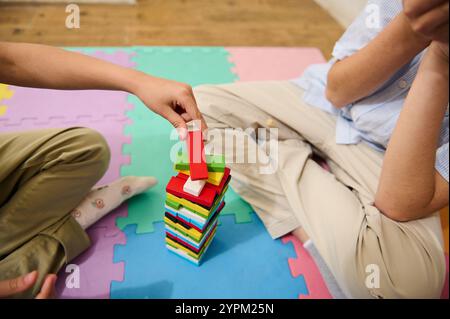 Zwei Kinder spielen eine lustige Aktivität und stapeln bunte Holzblöcke auf einer Schaumstoffmatte. Die Szene fängt das Wesen des Kinderspiels, der Kreativität und der ein Stockfoto