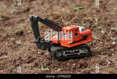Orangefarbenes Bagger- oder Baggerspielzeug graben Sie auf einem Boden im Freien. Modellmaßstab des Baggerfotos, Baukonzept. Stockfoto