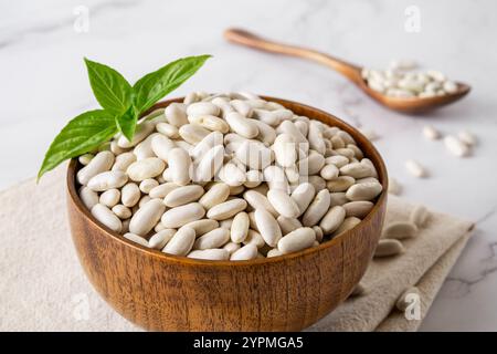 Nahaufnahme von weißen Kidneybohnen in einer Holzschale. Schüssel mit rohen trockenen weißen Bohnen, zubereitet zum Kochen von gebackenen Bohnen, Bohnensuppe, Kuchen. Pflanzenprotein, Ernte. Stockfoto