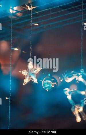 Zauberhafte Weihnachtsszene mit Blauhirsch, Glocke und baumförmigen Ornamenten, die vor Funkeln leuchten. Die bunten Lichter, die sich im Fenster spiegeln Stockfoto