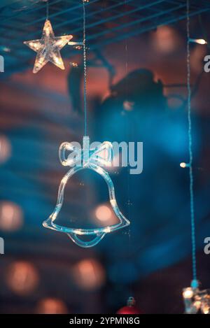 Zauberhafte Weihnachtsszene mit Blauhirsch, Glocke und baumförmigen Ornamenten, die vor Funkeln leuchten. Die bunten Lichter, die sich im Fenster spiegeln Stockfoto