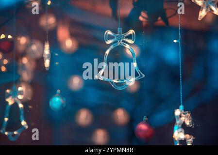 Zauberhafte Weihnachtsszene mit Blauhirsch, Glocke und baumförmigen Ornamenten, die vor Funkeln leuchten. Die bunten Lichter, die sich im Fenster spiegeln Stockfoto