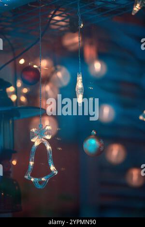 Zauberhafte Weihnachtsszene mit Blauhirsch, Glocke und baumförmigen Ornamenten, die vor Funkeln leuchten. Die bunten Lichter, die sich im Fenster spiegeln Stockfoto