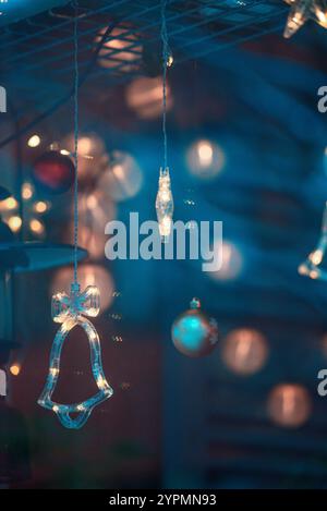Zauberhafte Weihnachtsszene mit Blauhirsch, Glocke und baumförmigen Ornamenten, die vor Funkeln leuchten. Die bunten Lichter, die sich im Fenster spiegeln Stockfoto