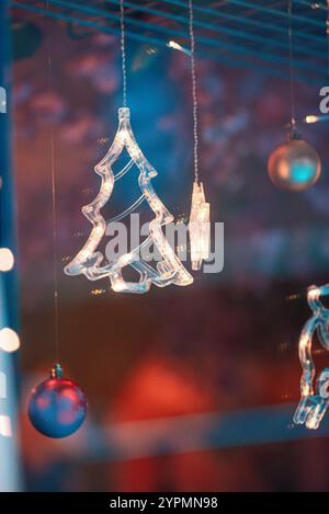 Zauberhafte Weihnachtsszene mit Blauhirsch, Glocke und baumförmigen Ornamenten, die vor Funkeln leuchten. Die bunten Lichter, die sich im Fenster spiegeln Stockfoto