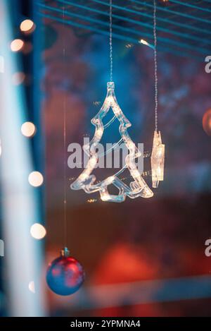 Zauberhafte Weihnachtsszene mit Blauhirsch, Glocke und baumförmigen Ornamenten, die vor Funkeln leuchten. Die bunten Lichter, die sich im Fenster spiegeln Stockfoto